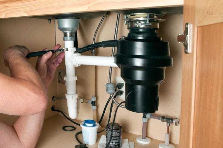 Plumber installing a garbage disposal beneath a kitchen sink in Lansdale